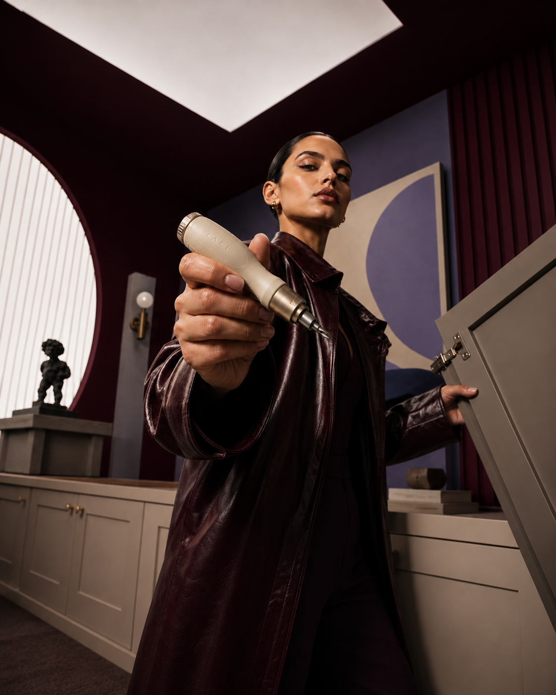 A woman in an oxblood leather coat holding the TAEL ratcheting screwdriver toward the camera.